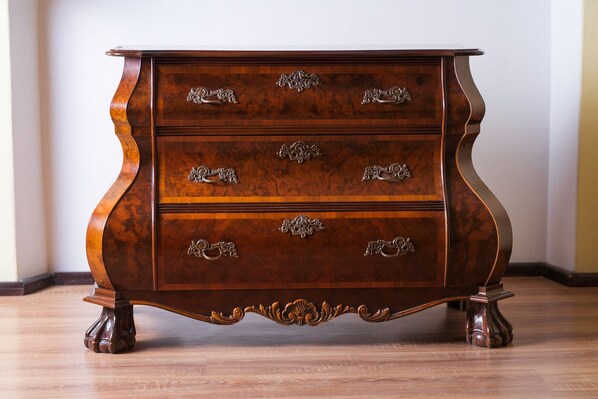 Une commode en bois, dotée de poignées métalliques décoratives et d’une base incurvée.