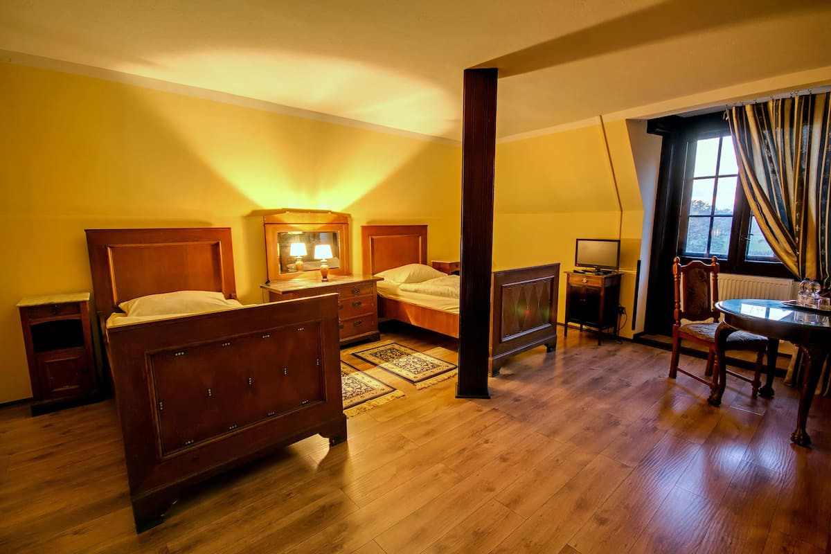 Een hotelkamer met een houten bed, nachtkastjes, een bureau met stoel, een televisie en een raam met gordijnen.