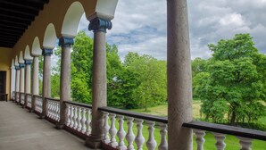 Un balcón cubierto con columnas y barandillas, que da a un paisaje verde con árboles.