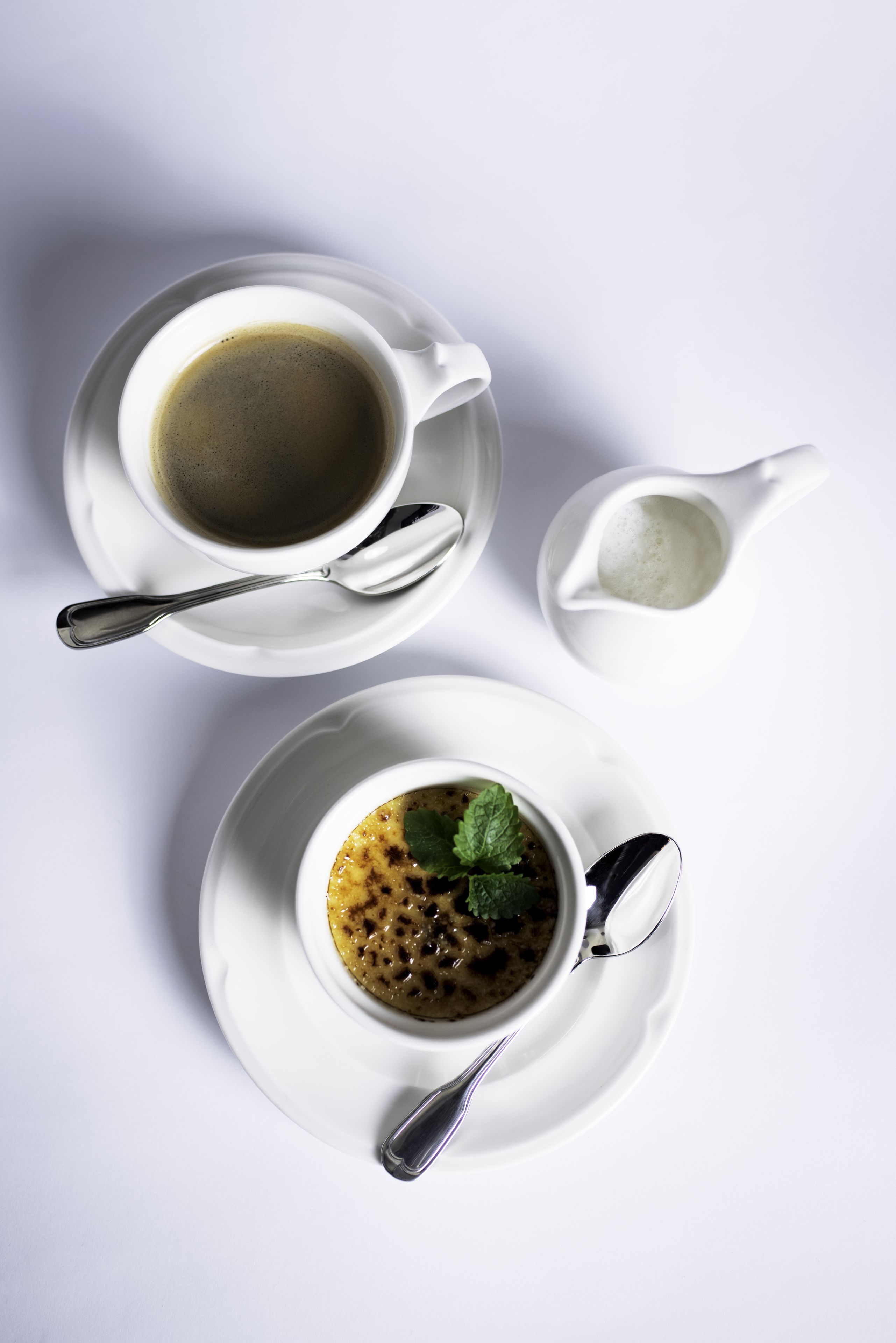 Una mesa blanca con una taza de café, un plato pequeño de sopa y un salero.