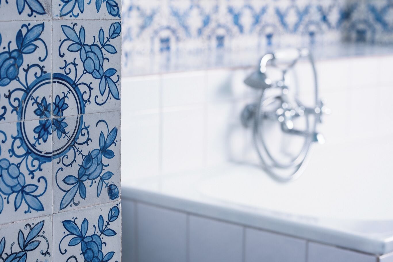 Casa de banho com azulejos florais azuis e uma banheira branca.