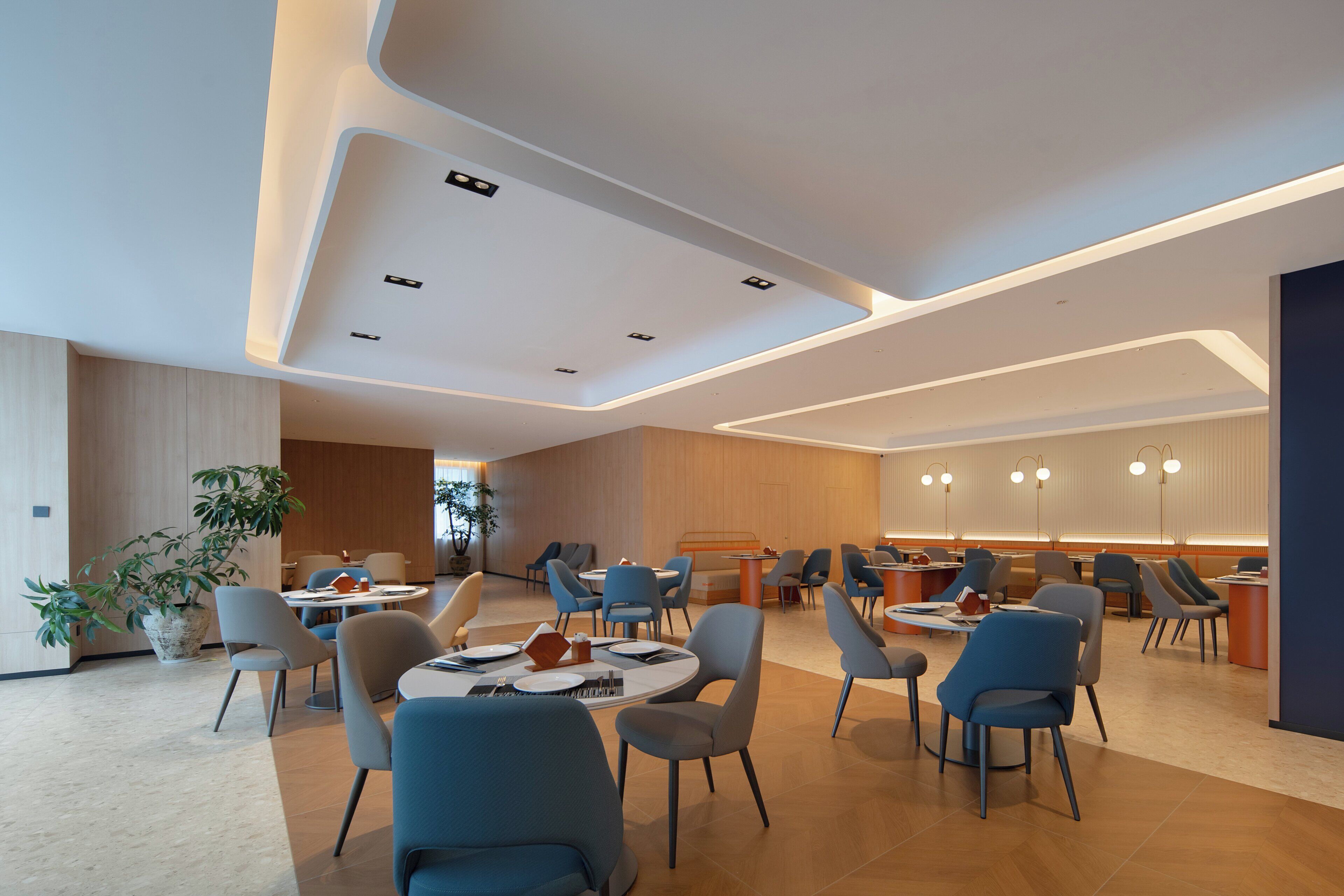 Uma sala de jantar moderna com mesas redondas, cadeiras azuis e iluminação embutida no teto.
