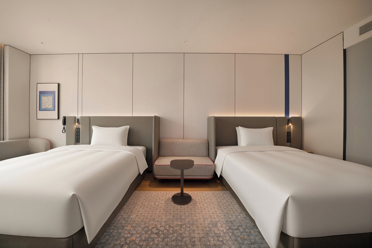 Ein Hotelzimmer mit zwei Betten, einem kleinen Tisch und einem an der Wand befestigten Telefon.