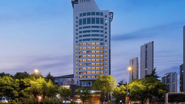 A tall, modern building with a clock tower, surrounded by trees and other buildings. - Holiday Inn Express Yiwu International Trade City by IHG (Jinhua)