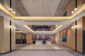 Eine moderne Hotelhalle mit einer Rezeption, einer hohen Decke und einem Zwischengeschoss.