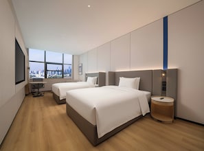 Quarto de hotel moderno com duas camas, uma mesa de trabalho e uma janela grande com vista para a cidade.