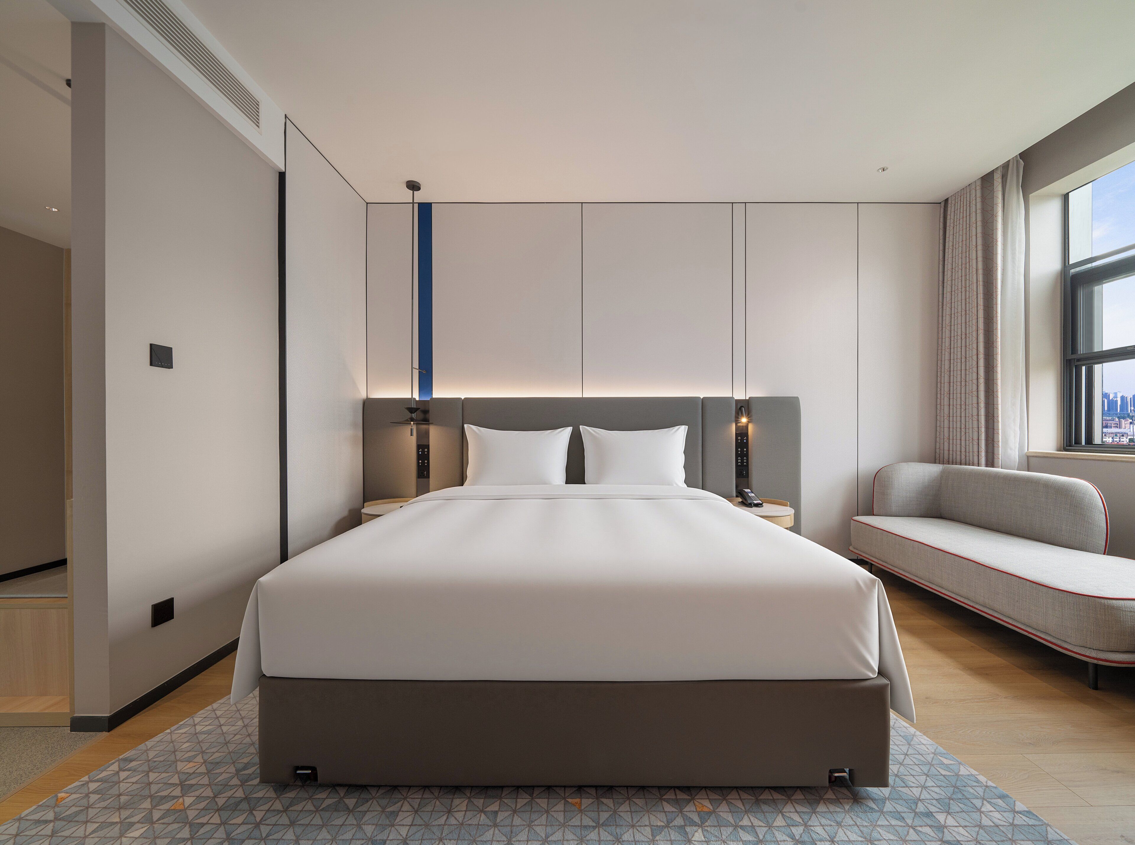 Ein modernes Hotelzimmer mit einem großen Bett, einer Sitzecke, einem Schreibtisch und Blick auf die Stadt.