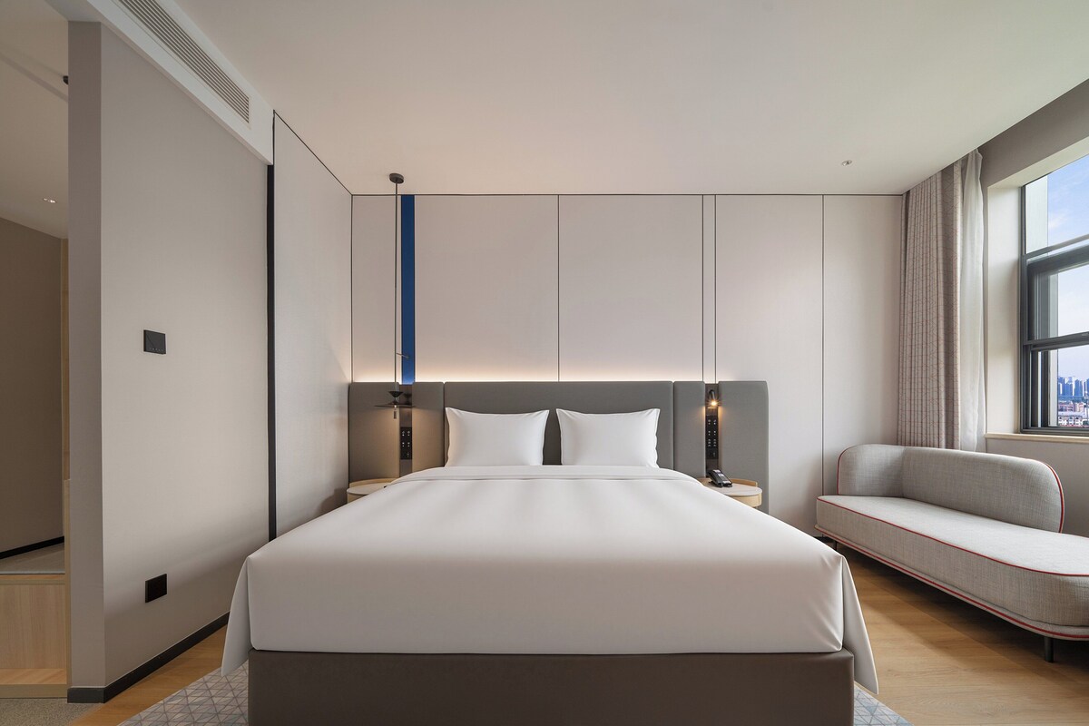 Ein modernes Hotelzimmer mit einem großen Bett, einer Sitzecke, einem Schreibtisch und Blick auf die Stadt.