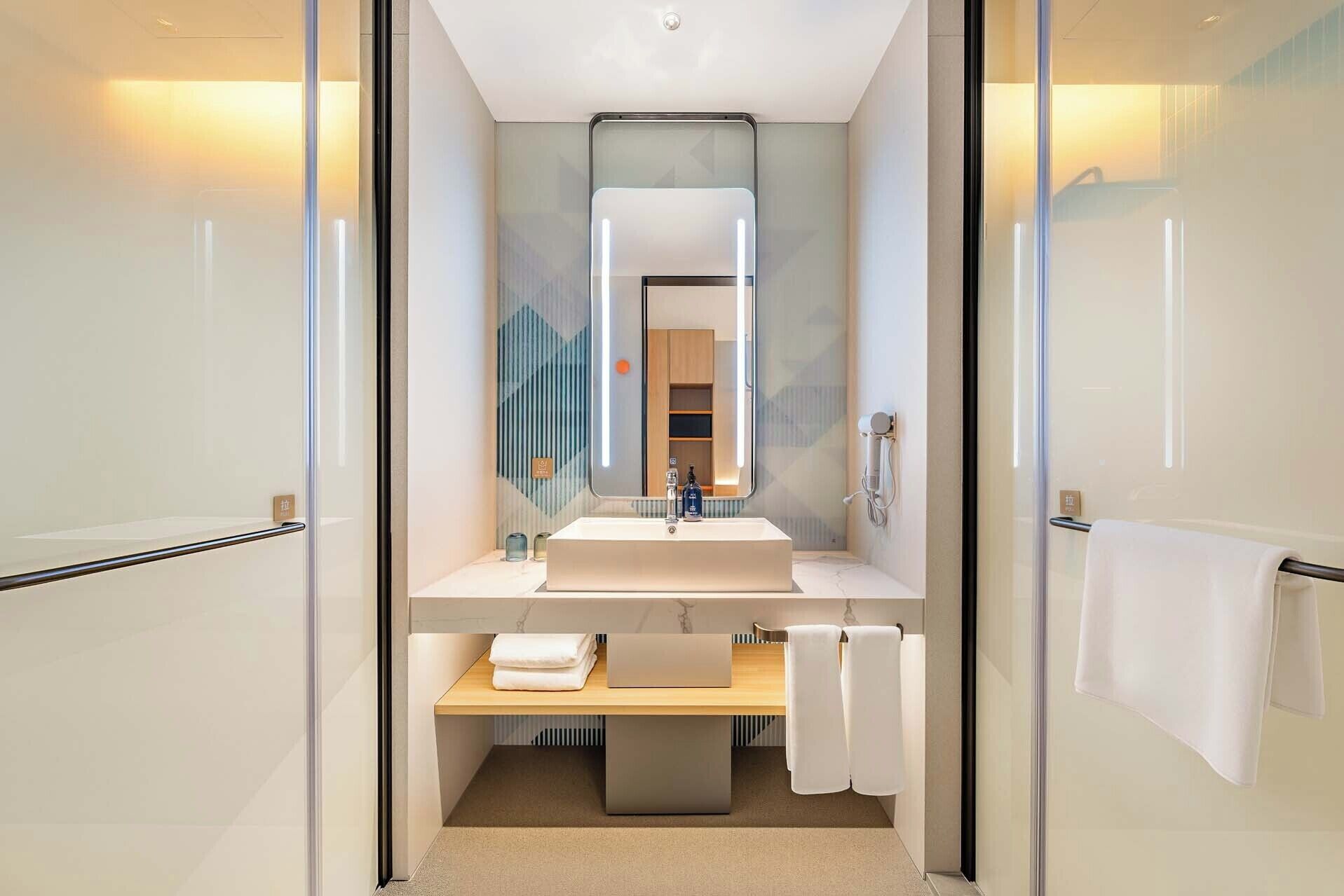 Un baño moderno con puerta de vidrio, lavamanos, espejo y toallero.