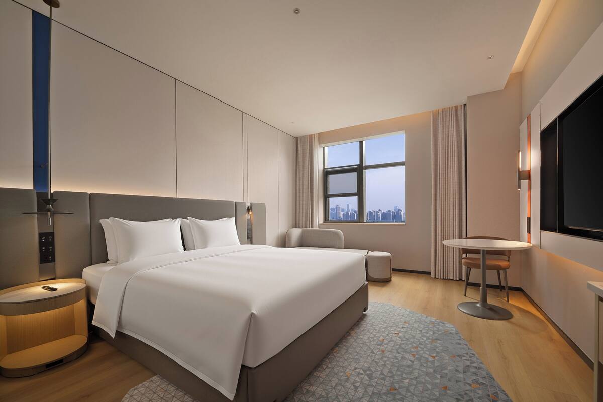 Ein modernes Hotelzimmer mit einem großen Bett, Nachttischen, einem Schreibtisch und Blick auf die Stadt.
