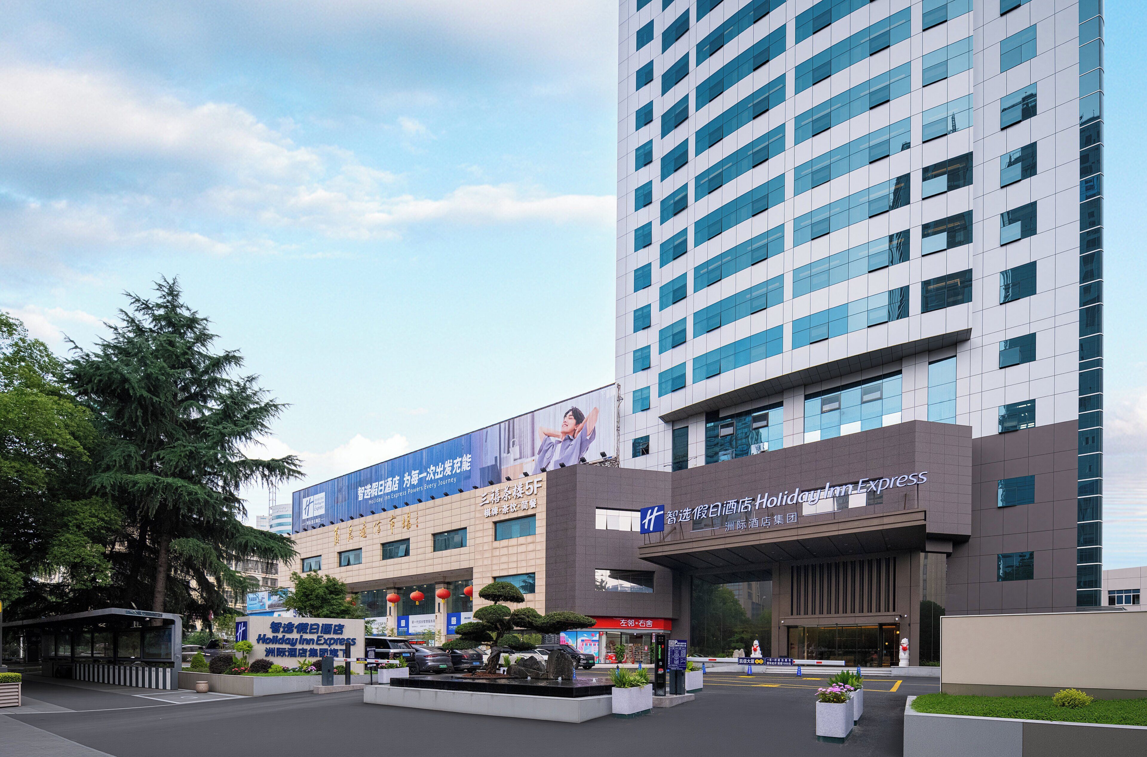 Edificio de Holiday Inn Express con fachada moderna, ventanas amplias y zona de entrada ajardinada.