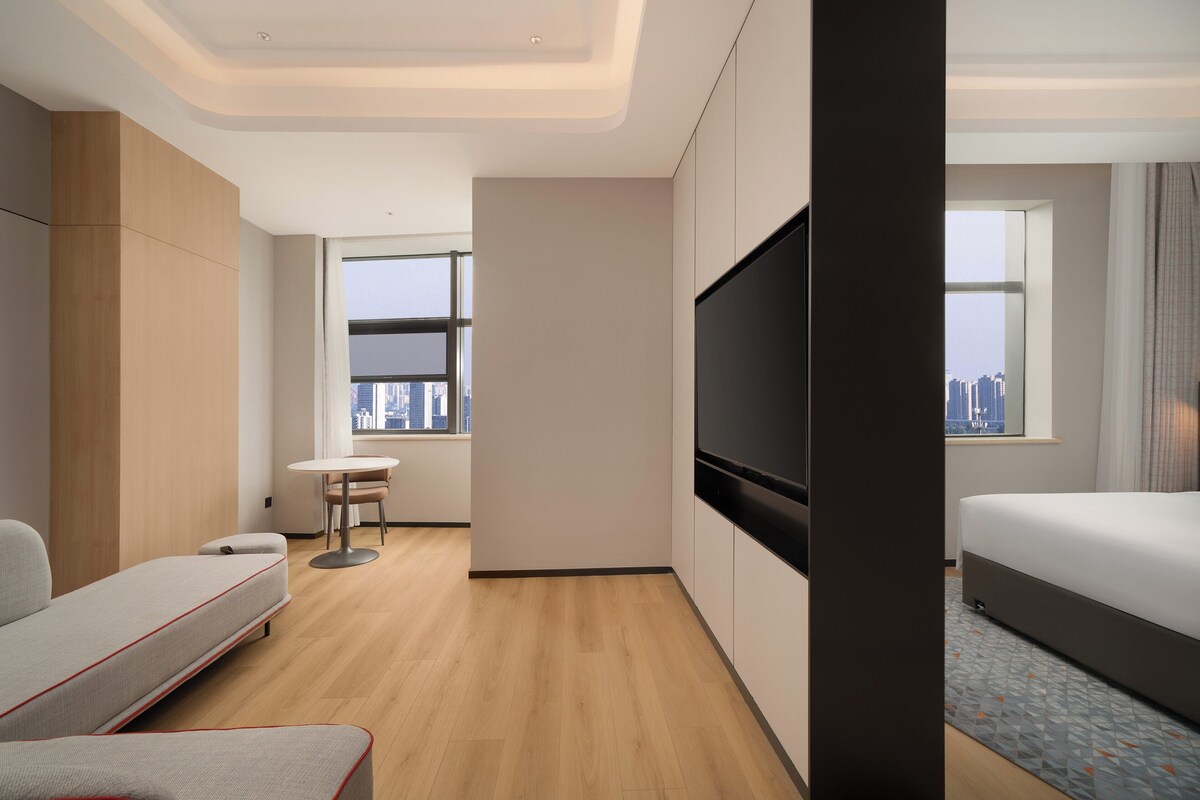 Ein modernes Hotelzimmer mit einer Couch, einem Fernseher, einem kleinen Tisch und Blick auf die Stadt.