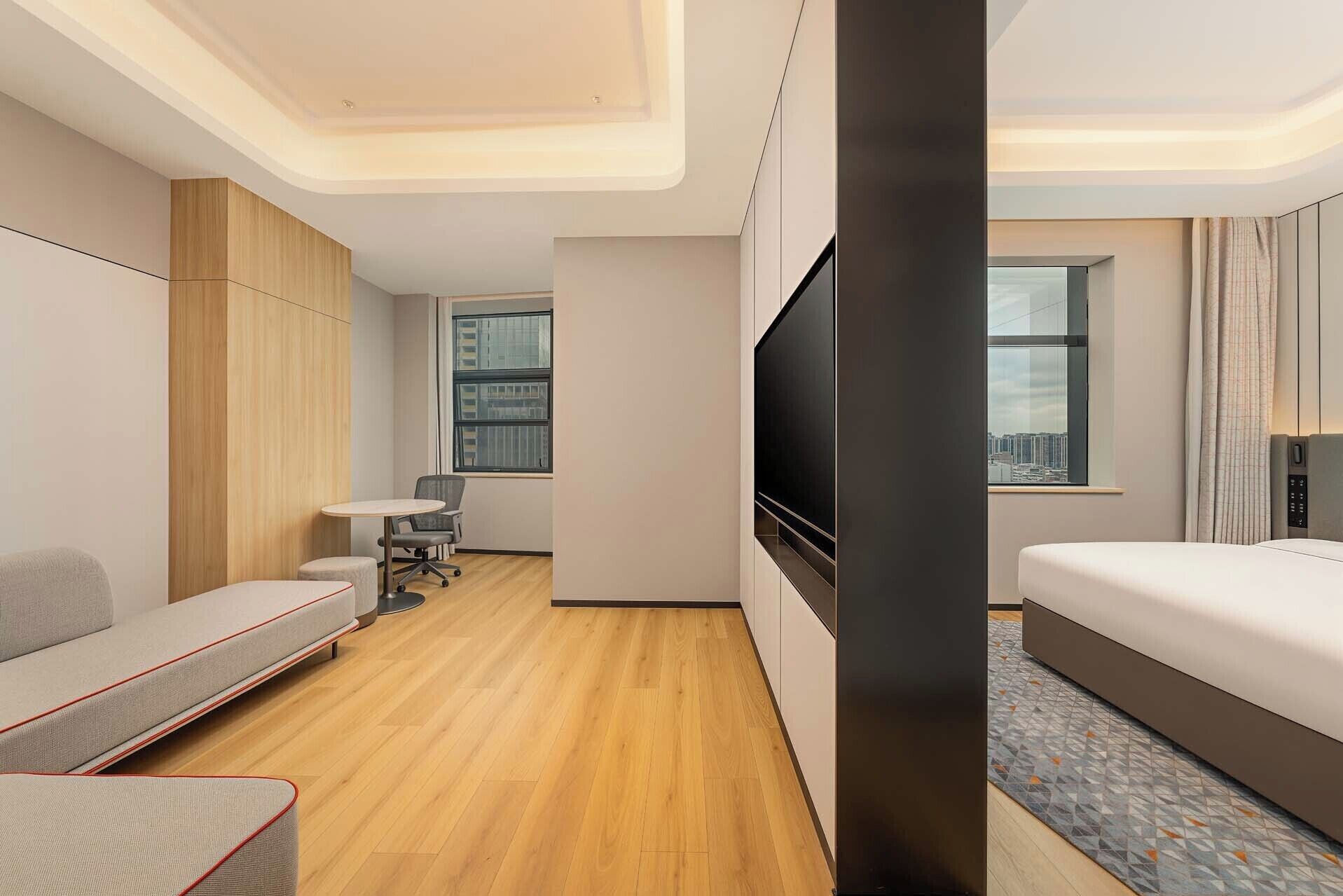 Habitación de hotel moderna con sofá, cama, televisión y vistas a la ciudad.