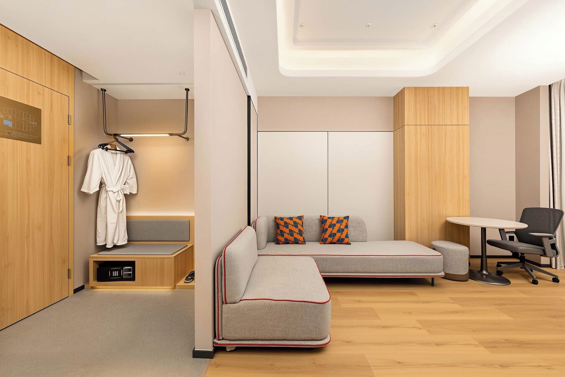 Una habitación de hotel moderna con sofá cama, escritorio, silla, armario y zona de ducha.