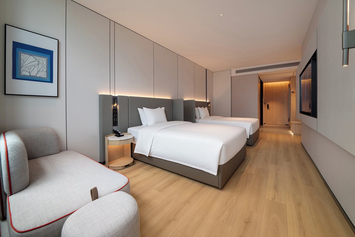 Ein modernes Hotelzimmer mit zwei Betten, einem Schlafsofa, einem Nachttisch mit Telefon und einem gerahmten Bild an der Wand.