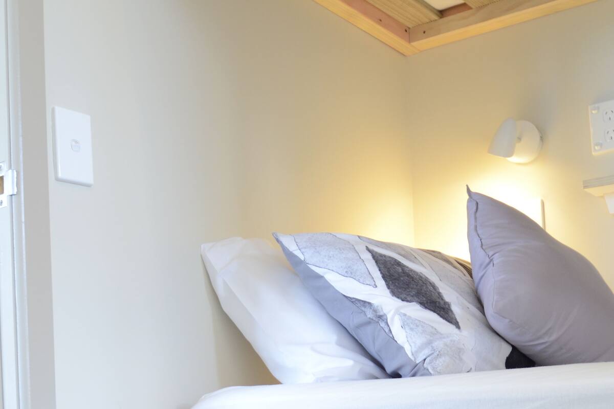 A bedroom with a bed, pillows, a wall-mounted light, and a door.