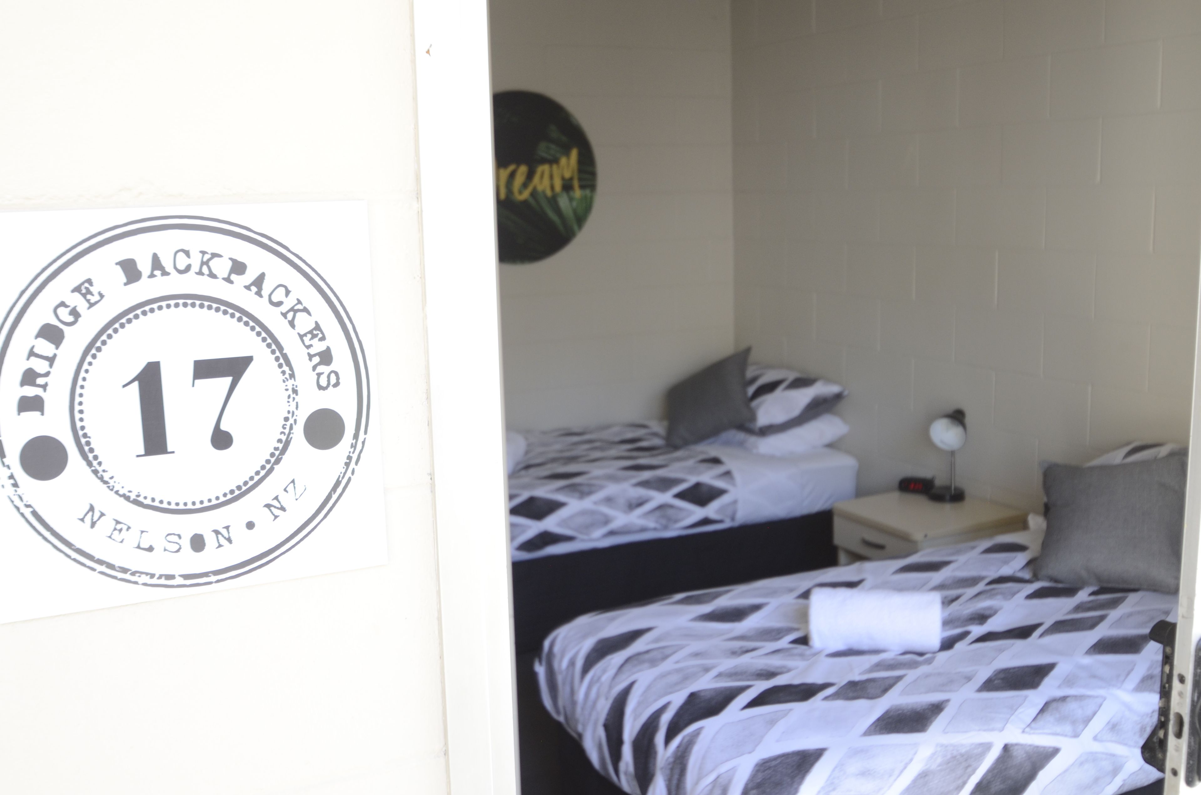 Una habitación con dos camas, cada una con una colcha estampada. Hay un cartel en la pared que dice "Bridge Backpackers" y el número "17".