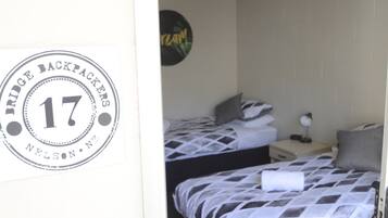 Una habitación con dos camas, cada una con una colcha estampada. Hay un cartel en la pared que dice "Bridge Backpackers" y el número "17".