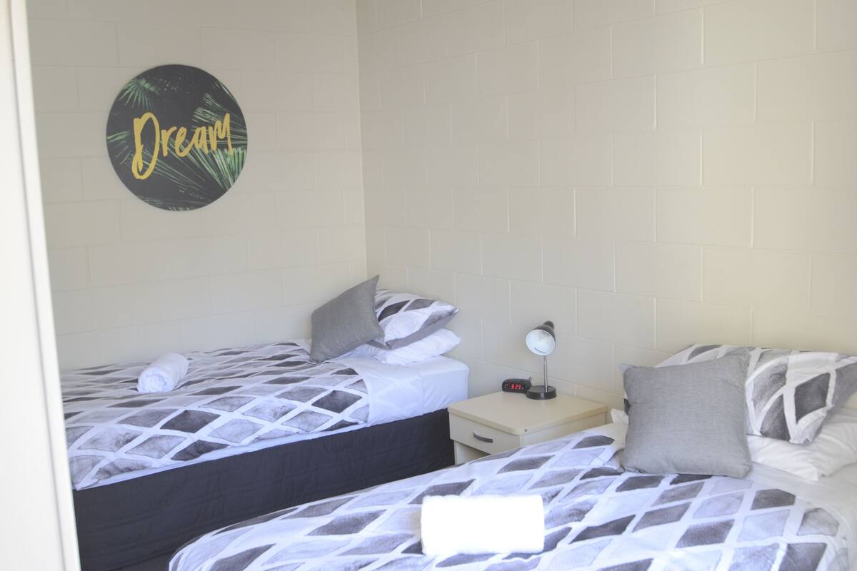 A room with two beds, a nightstand with a clock, and a wall with a circular sign.