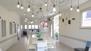 A spacious, well-lit dining area with a long table and chairs, a kitchen in the background, and a colorful sofa in the foreground. - Bridge Backpackers (Nelson)