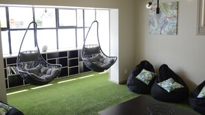 A room with two hanging chairs, a bean bag area, and a geometric art piece on the wall. - Bridge Backpackers (Nelson)