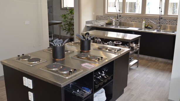 A modern kitchen with stainless steel appliances, a central island with a sink, and a view of the adjacent dining area. - Bridge Backpackers (Nelson)