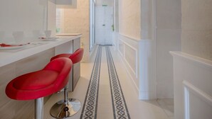 A narrow hallway with a tiled floor, a white reception desk, and red bar stools. - Valletta Rodrigo Apartment (Valletta)