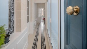 A hallway with patterned floor tiles, a blue door with a brass handle, and a white ceiling light. - Valletta Rodrigo Apartment (Valletta)