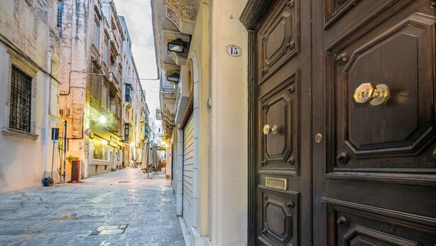 A narrow street with a dark wooden door on the right and a building with a number '15' sign on the left. - Valletta Rodrigo Apartment (Valletta)