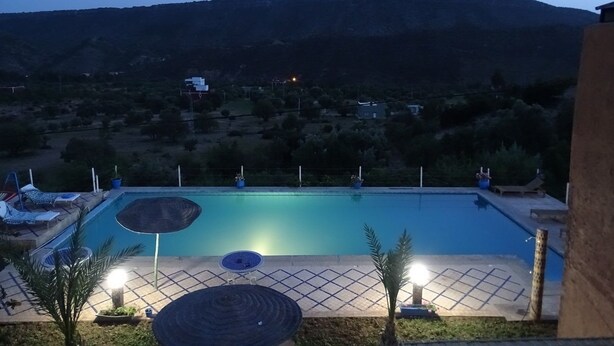 A swimming pool with lounge chairs and umbrellas, surrounded by a landscaped area with a mountain in the background.