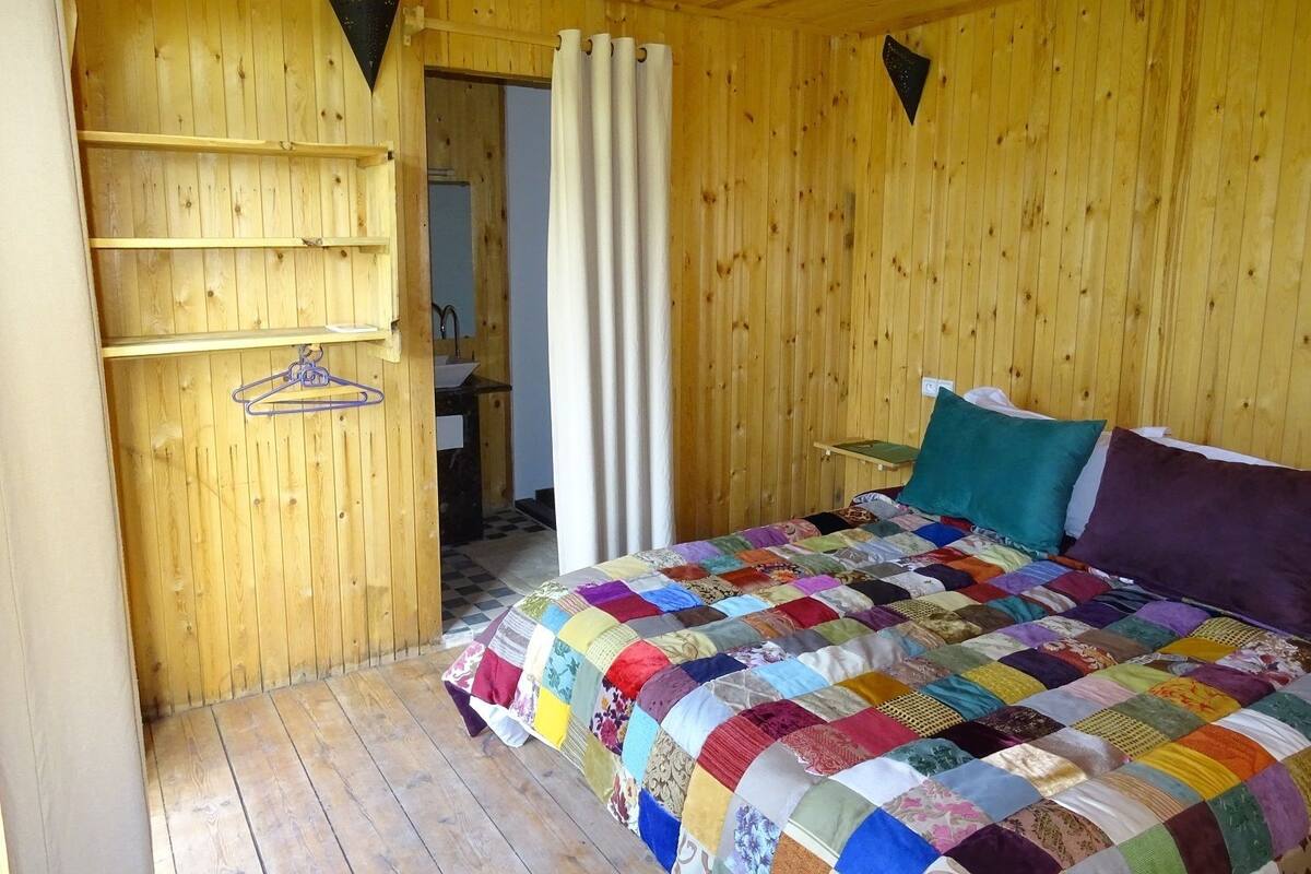 A wooden room with a bed, a shelf with hangers, and a door leading to a bathroom.