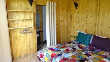 A wooden room with a bed, a shelf with hangers, and a door leading to a bathroom.