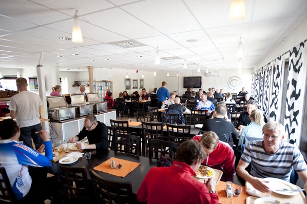 A cafeteria with multiple tables and chairs, equipped with kitchen appliances and a television screen. - Valbergsängen Hotell & Vandrarhem (Torsby)