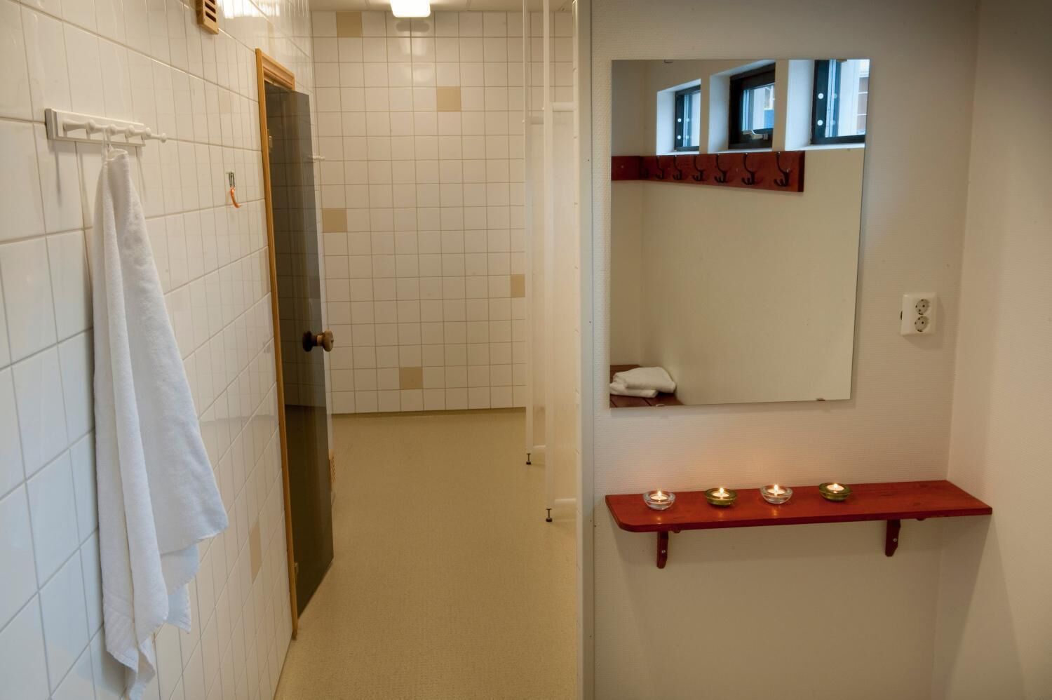A bathroom with white tiled walls, a glass door, a towel rack, a mirror, and a shelf with candles.
