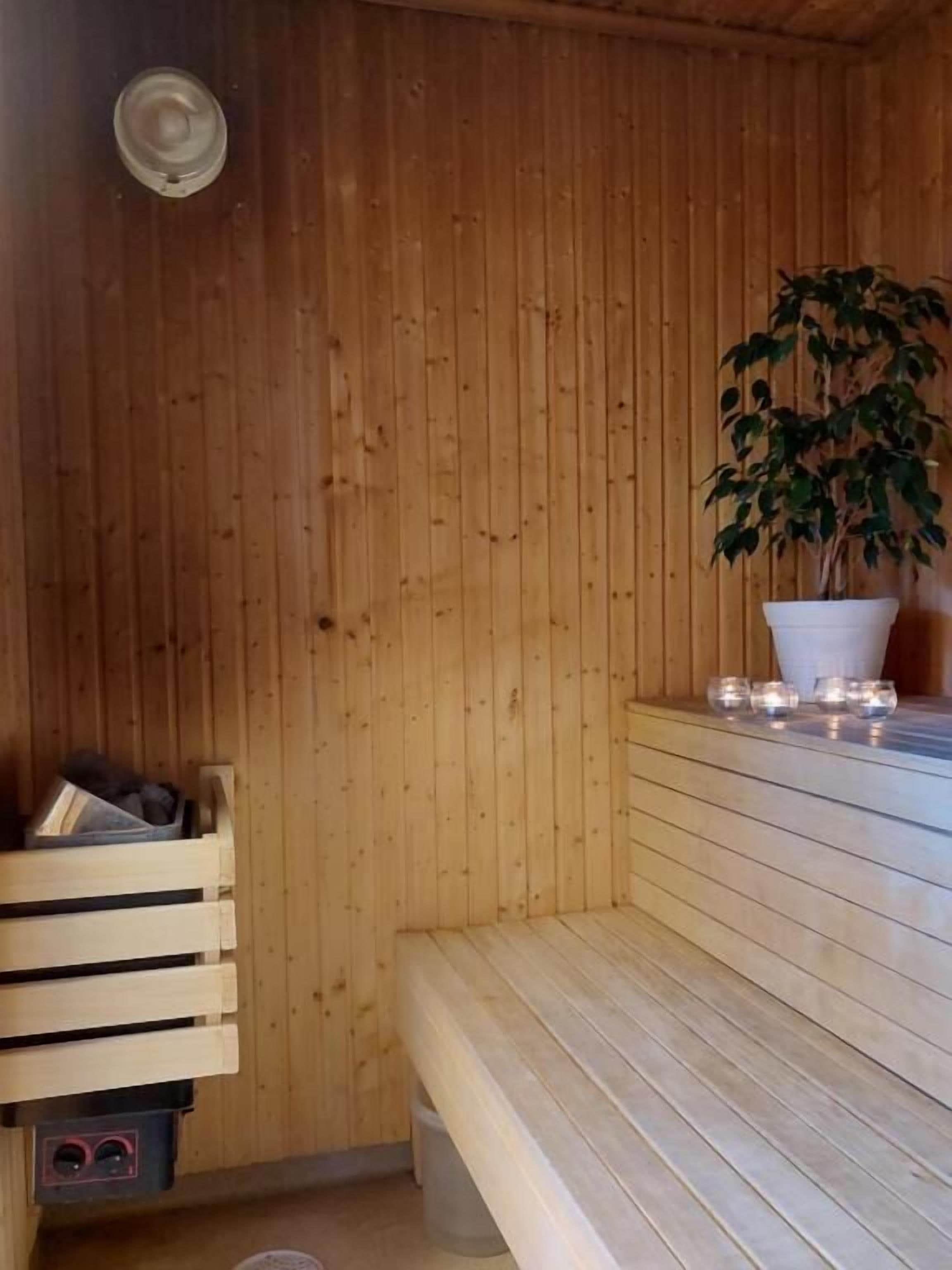 Un sauna con paredes de madera, un banco, una planta en maceta y un pequeño estante con velas.