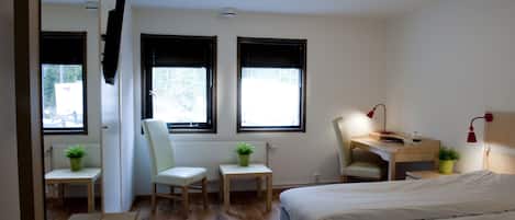 Un dormitorio con cama, escritorio, dos sillas, radiador y ventana.