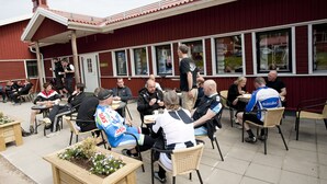 Ulkoterassi, jossa on pöytiä ja tuoleja, rakennus suurilla ikkunoilla ja punainen julkisivu.