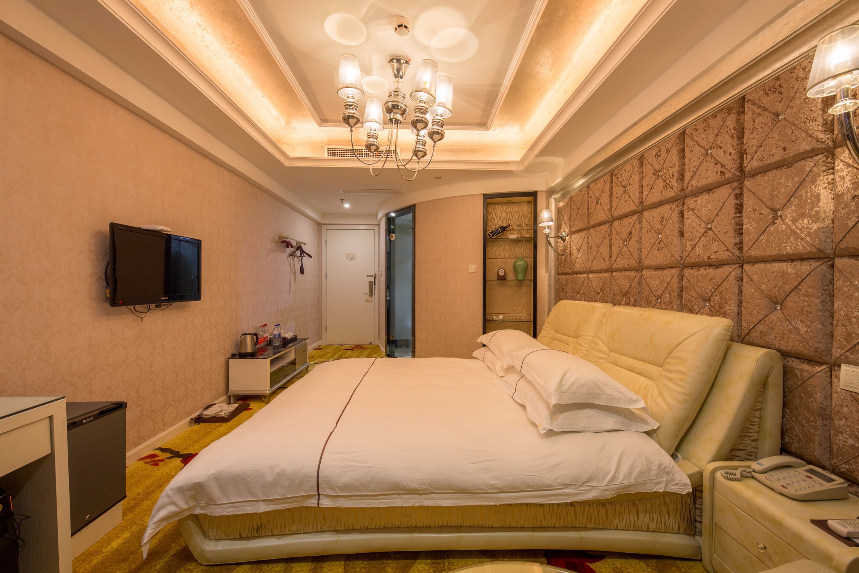 Hotelkamer met een groot bed, een aan de muur bevestigde televisie, een nachtkastje met telefoon en een vloerbedekking.