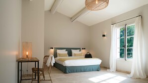 Un dormitorio con cama, mesita de noche, silla y ventana con cortinas.