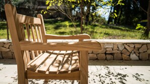 Un banco de madera con asientos de listones, ubicado al aire libre frente a un muro de piedra y follaje.