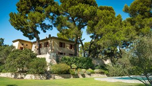 Una villa de estilo mediterráneo con un muro de piedra, una piscina y abundante vegetación.