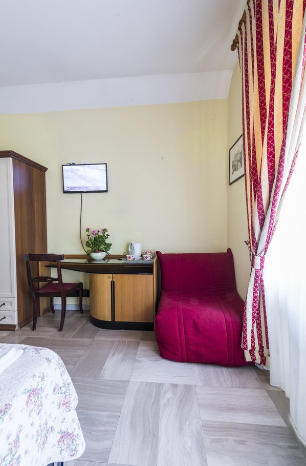 A room with a bed, a desk with a computer, a chair, a red sofa, and a TV on the wall.