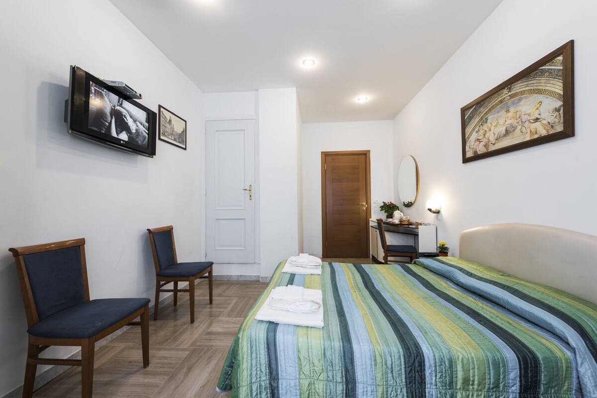Ein Hotelzimmer mit einem Bett, zwei Stühlen, einem Fernseher, einem Gemälde und einer Tür.
