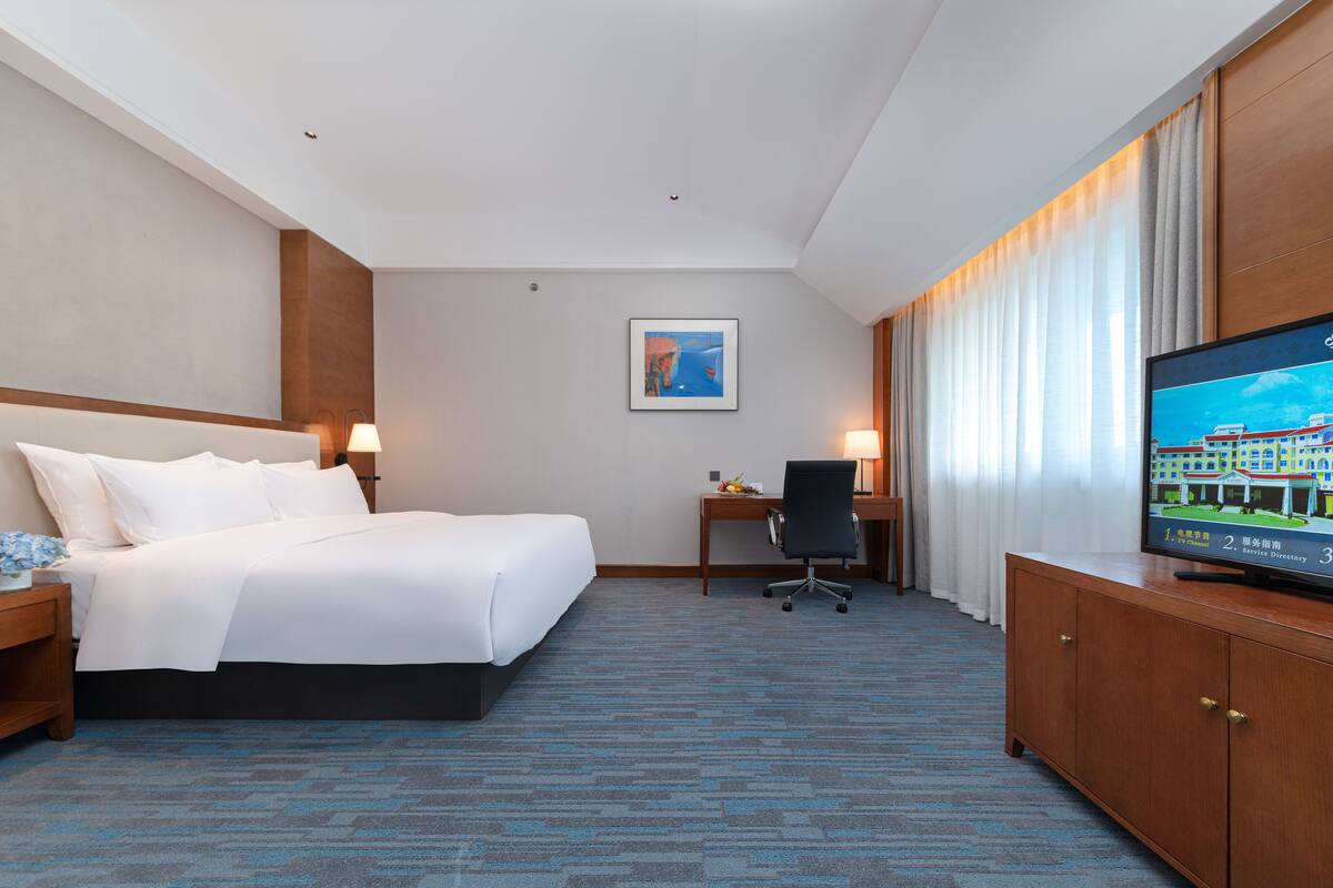Ein Hotelzimmer mit Bett, Schreibtisch, Stuhl, Fernseher und Vorhängen.