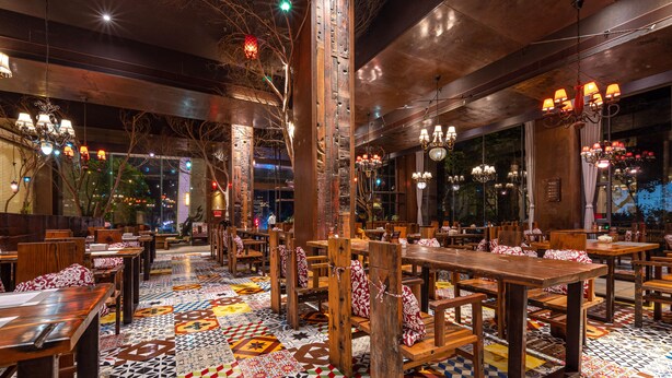A restaurant with wooden tables and chairs, patterned floor tiles, and hanging chandeliers. - Yihohotel Xiang'An Xiamen (Xiamen)
