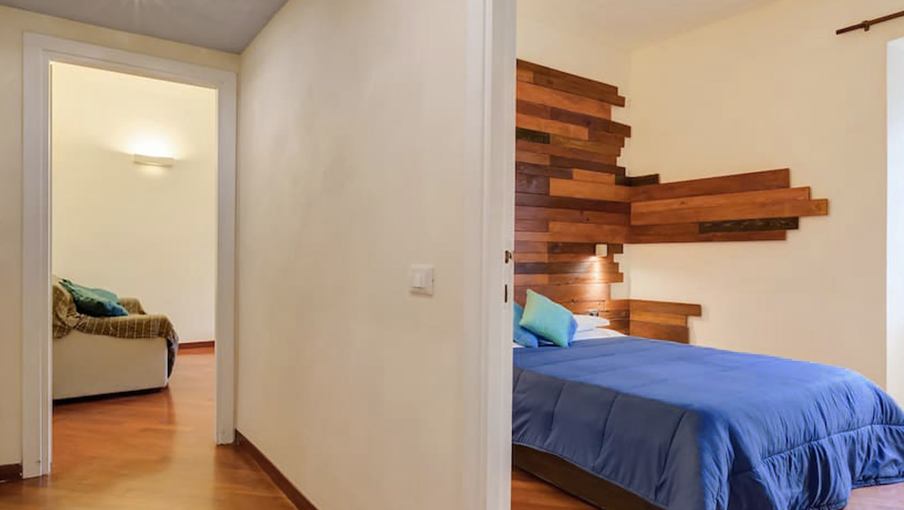 A bedroom with a wooden headboard, a bed with blue bedding, and a small seating area with a chair and cushions.