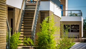 Un bâtiment moderne doté d’un escalier menant à un balcon, le tout entouré de verdure.