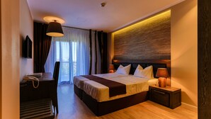 Une chambre d’hôtel moderne avec un grand lit, des lampes de chevet, un bureau avec un téléphone et une vue sur l’extérieur par la fenêtre.