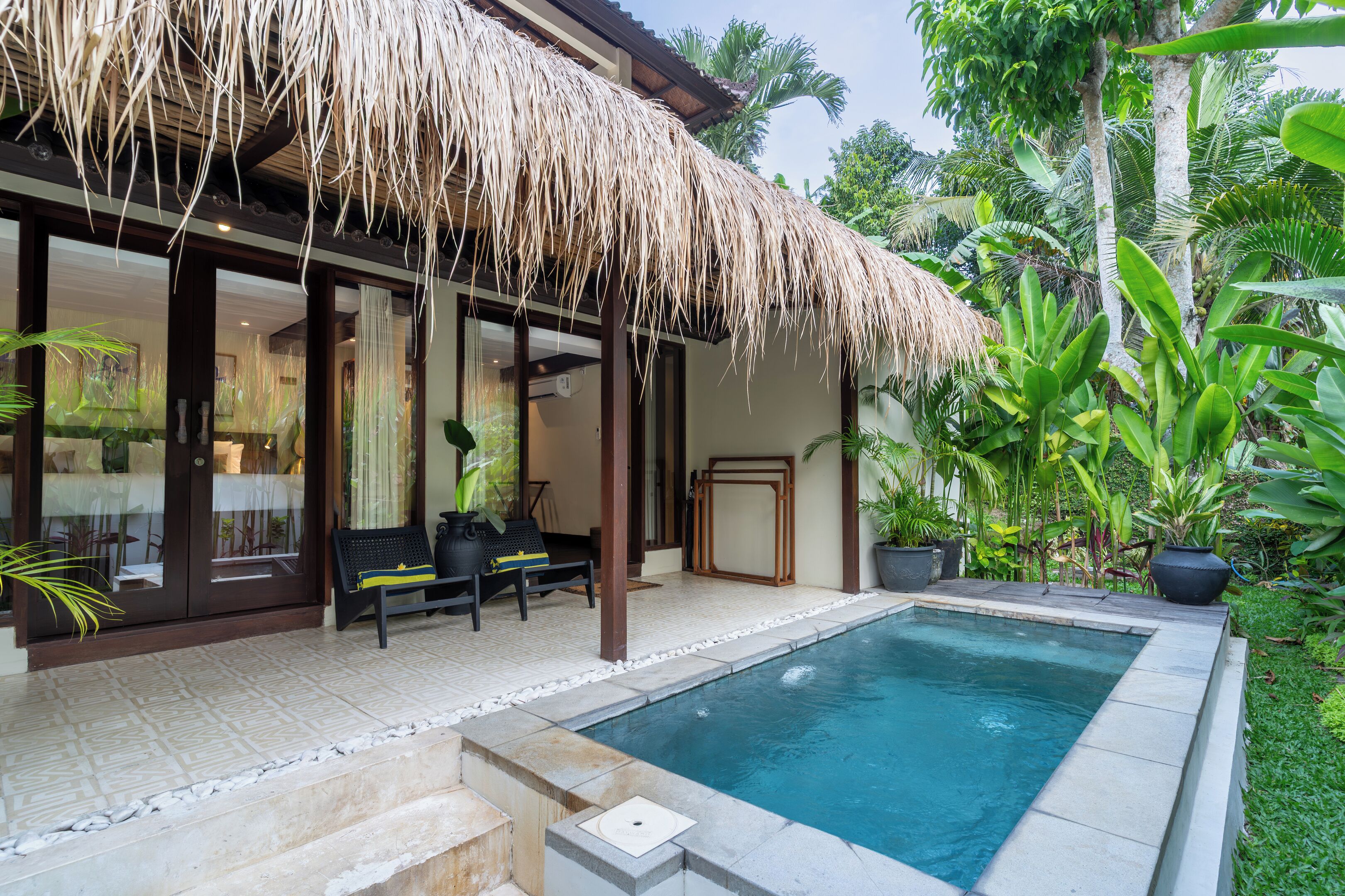 A poolside area with a thatched roof, a seating area with a bench, and a potted plant.