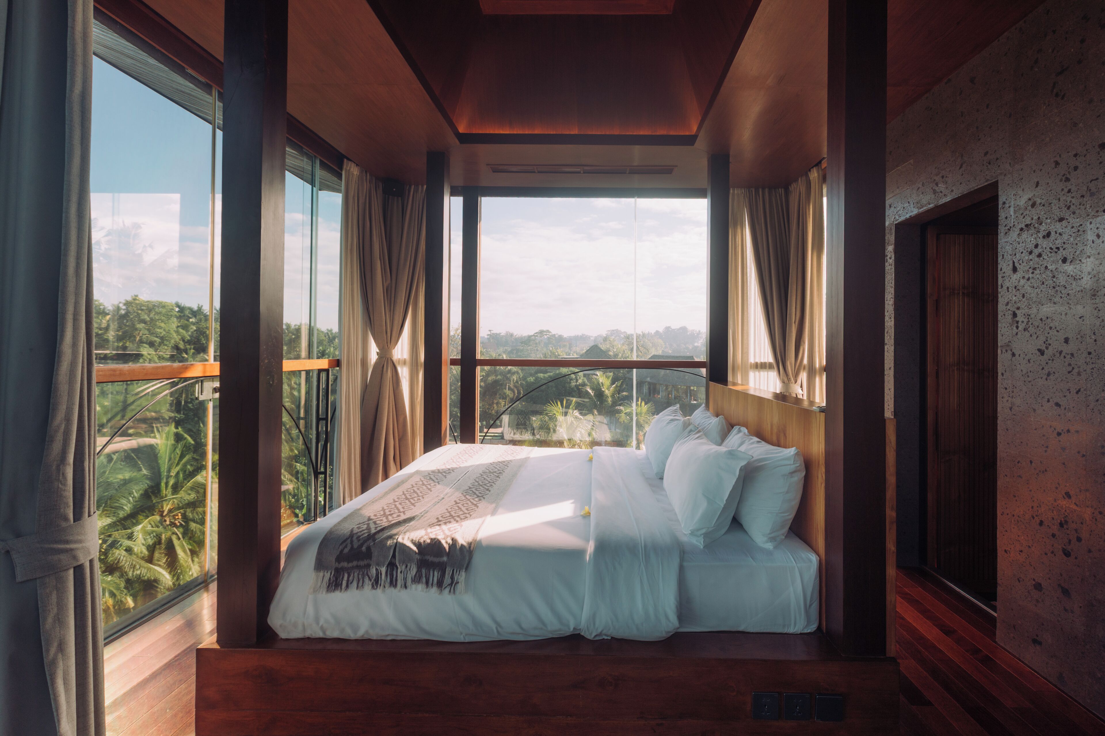 A large bed with a view of a tropical landscape through large windows.